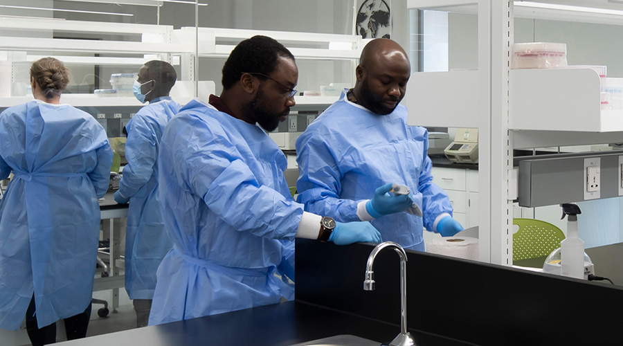 People in a laboratory wearing blue lab gowns and gloves.