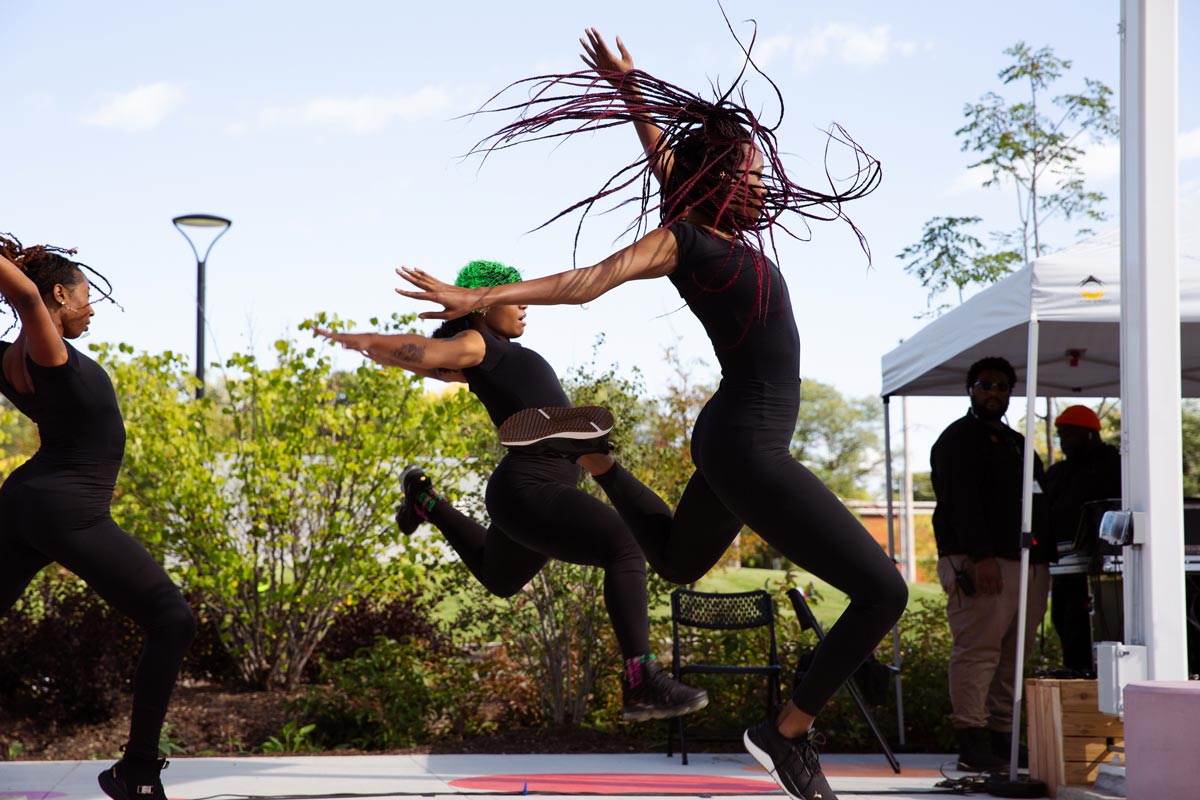 a sideview of three young women performing a dance, wearing all black leotards