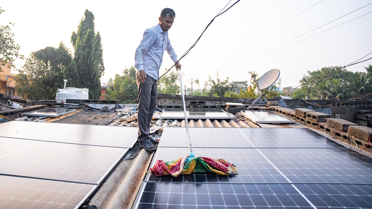 Man cleaning solar panels on a rooftop with a cloth mop on a stick.