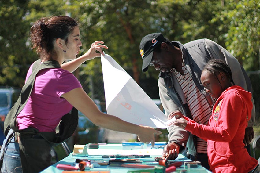 A woman holds a letterpress printed paper out for a man and young girl to look at.