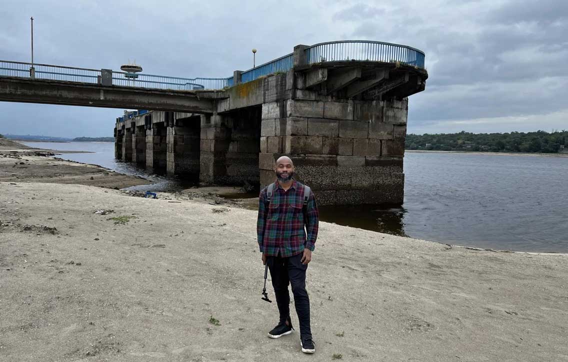 A man standing on the sand in front of a river