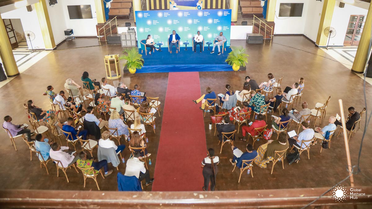 An overhead view of a large room with a 4 person panel on stage and members of the audience seated on chairs.