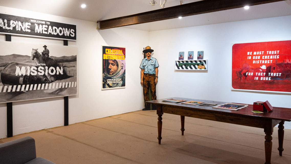 photos of Whit Montgomery's Alpine Meadows art installation, paintings on a white gallery wall with a table in front.